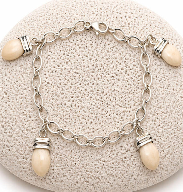 pulsera eslabones con 4 perlas de venado naturales colgando encima de una roca