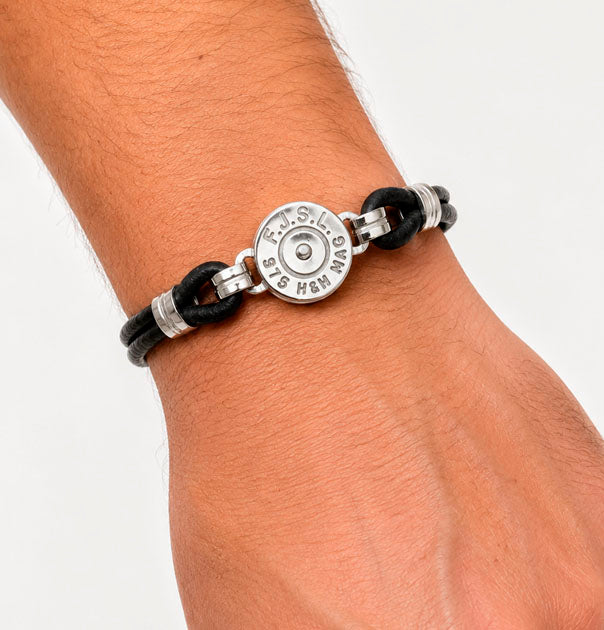 Detalle de réplica de culata de bala grabada con iniciales y calibre en pulsera de cuero y plata en la muñeca del modelo